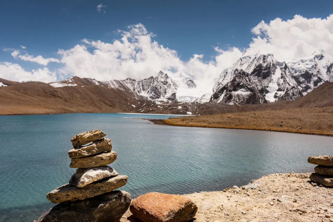 A high-altitude lake with stacked stones below snow peaks in Sikkim